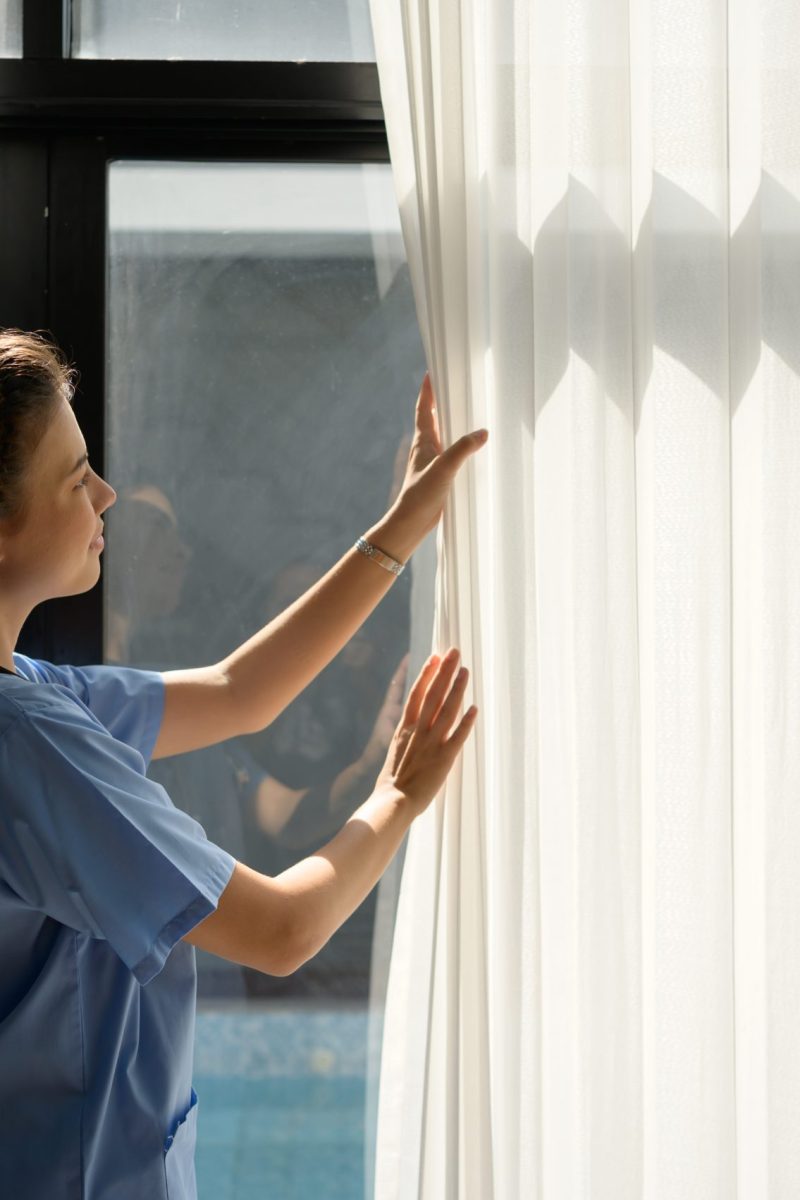 Asian nurse open the curtains in the living room to allow light to reach the room before bringing the patient to sit in this living room.