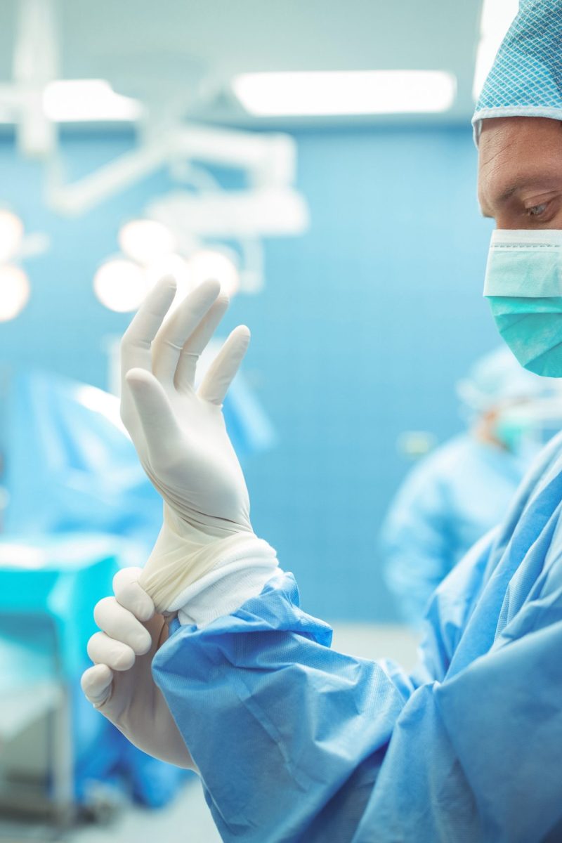 Male surgeon wearing surgical gloves in operation theater at hospital